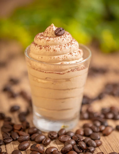 Crema fredda al caffè in bicchiere, decorata con chicco di caffè e polvere, chicchi sparsi sul tavolo