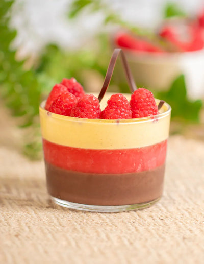 Dessert al bicchiere con strati di cioccolato, frutta e crema, decorato con lamponi freschi