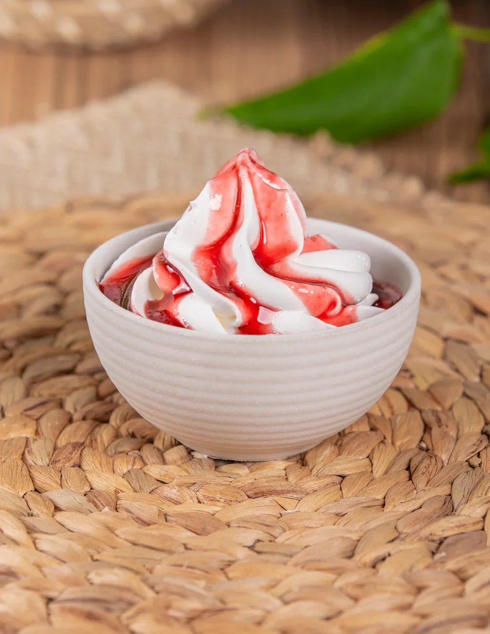 Coppa di gelato soft con topping alla fragola, presentata in una ciotola bianca su tovaglietta intrecciata.