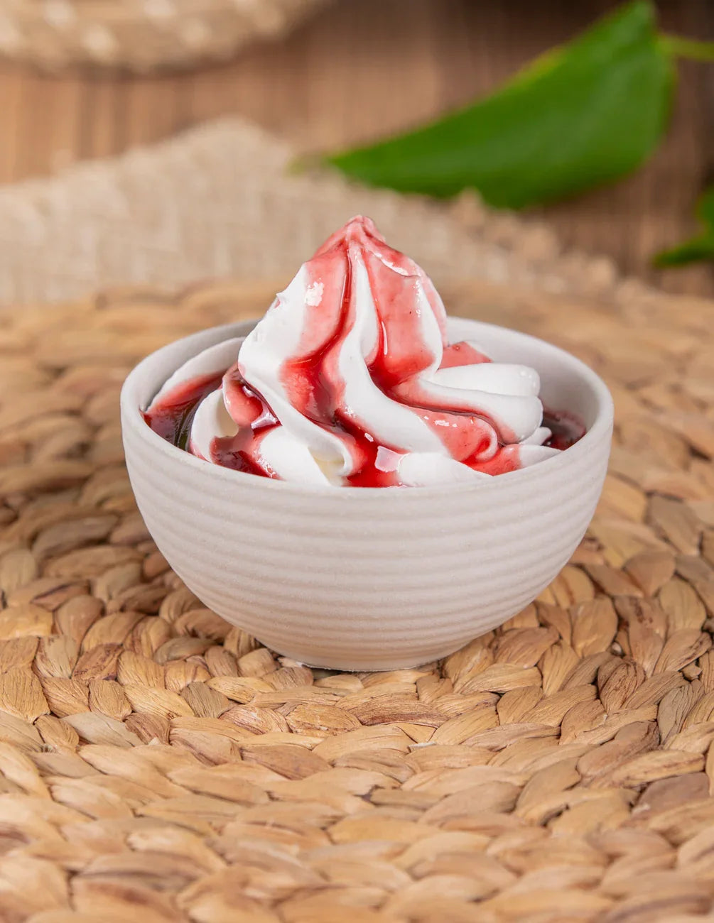 Frozen yogurt con salsa ai frutti di bosco in ciotola bianca su fondo intrecciato naturale.