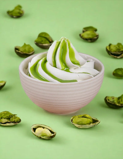 Coppa di gelato alla vaniglia con topping di pistacchio e pistacchi sgusciati su sfondo verde.