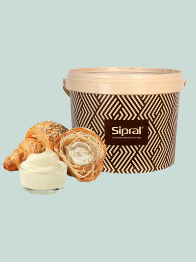 Crema bianca in ciotola e croissant ripieni davanti a secchiello per ingredienti dolci, fondo chiaro