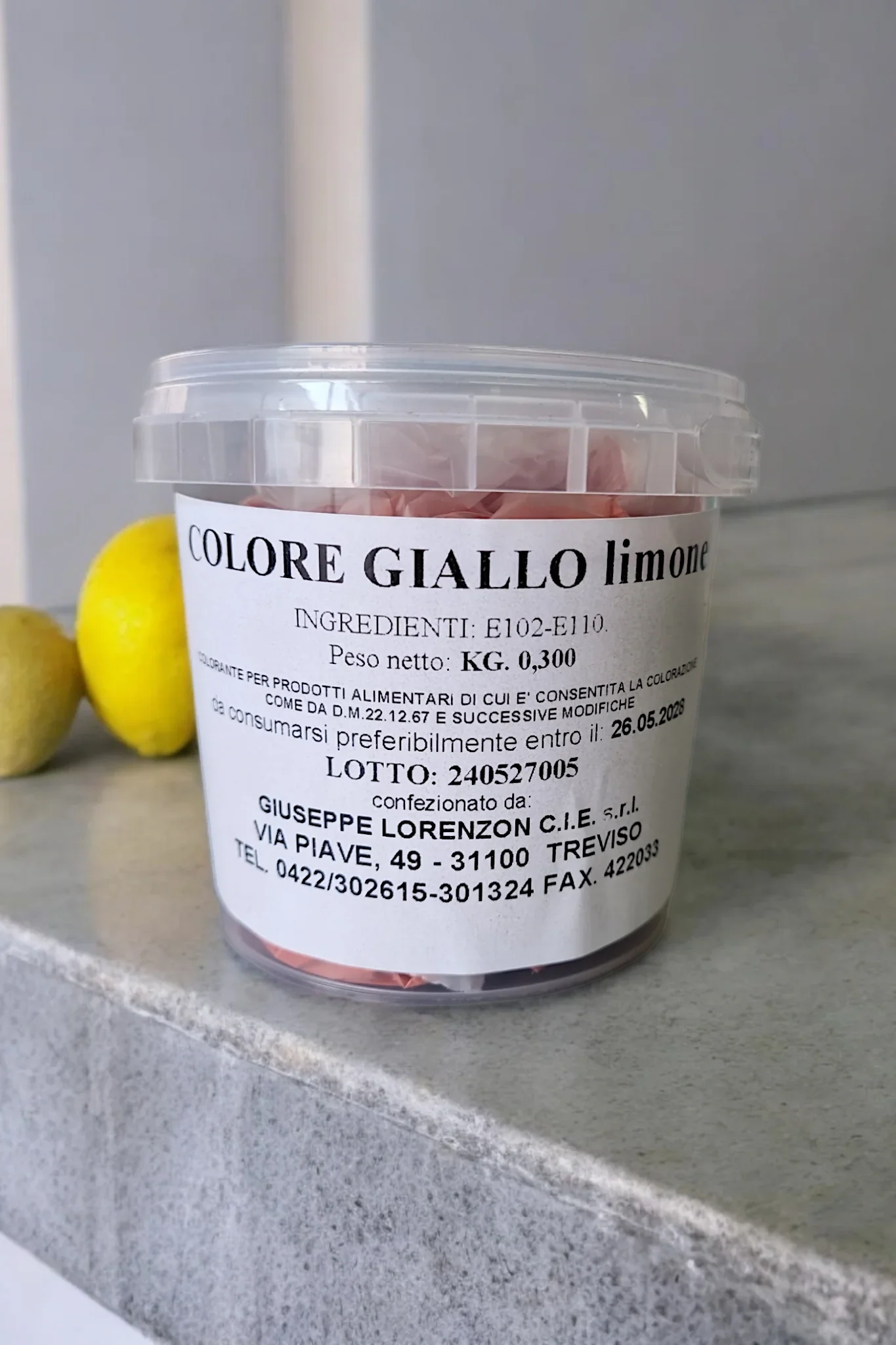 Barattolo di colorante alimentare giallo limone per dolci e pasticceria, con limoni sullo sfondo