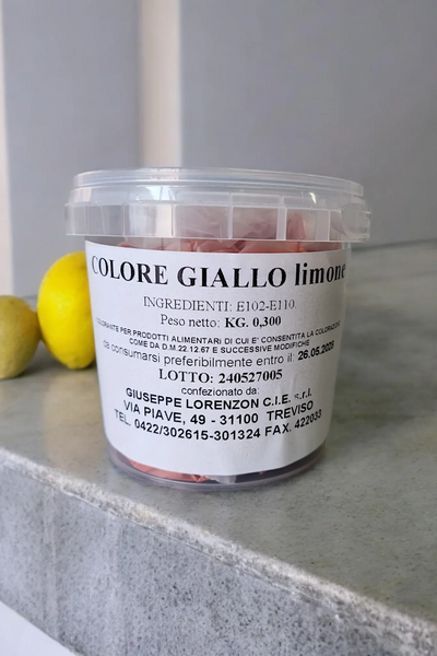 Barattolo di colorante alimentare giallo limone per dolci e pasticceria, con limoni sullo sfondo