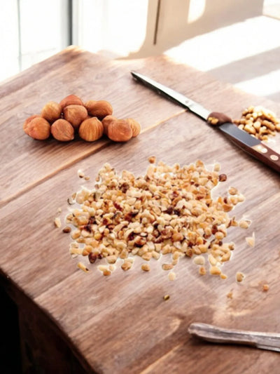 Granella di nocciole tostate su tagliere di legno con nocciole intere e coltello, ingrediente per dolci e gelato