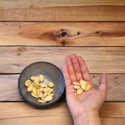 Mandorle pelate italiane in una ciotola e su una mano su fondo di legno, ingredienti per pasticceria.