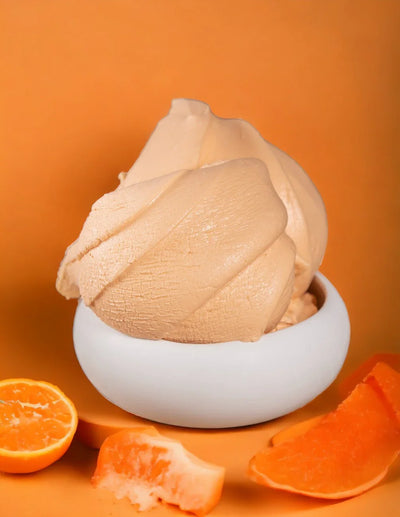 Gelato artigianale al melone in ciotola bianca con fette di melone e arancia, sfondo arancione