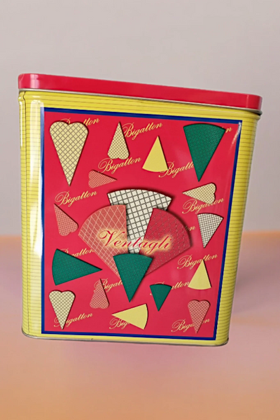 Scatola di latta decorata per ventagli biscotto, sfondo rosso e dettagli geometrici colorati.