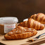 Croissant farcito con crema caramello mou salato e granelli di sale su tagliere, vasetto di crema sullo sfondo